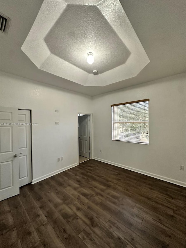 unfurnished bedroom featuring baseboards, visible vents, a tray ceiling, and dark wood-type flooring