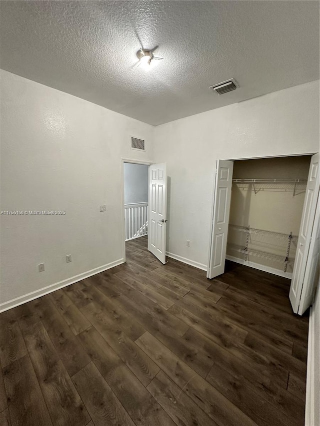 unfurnished bedroom with dark wood-style floors, a closet, and visible vents