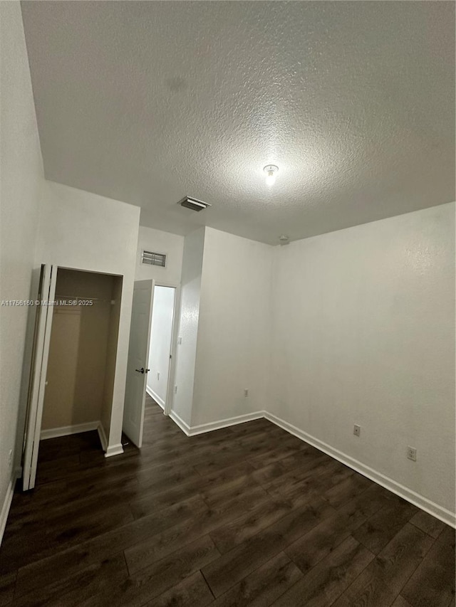 unfurnished room featuring dark wood-style floors, visible vents, a textured ceiling, and baseboards