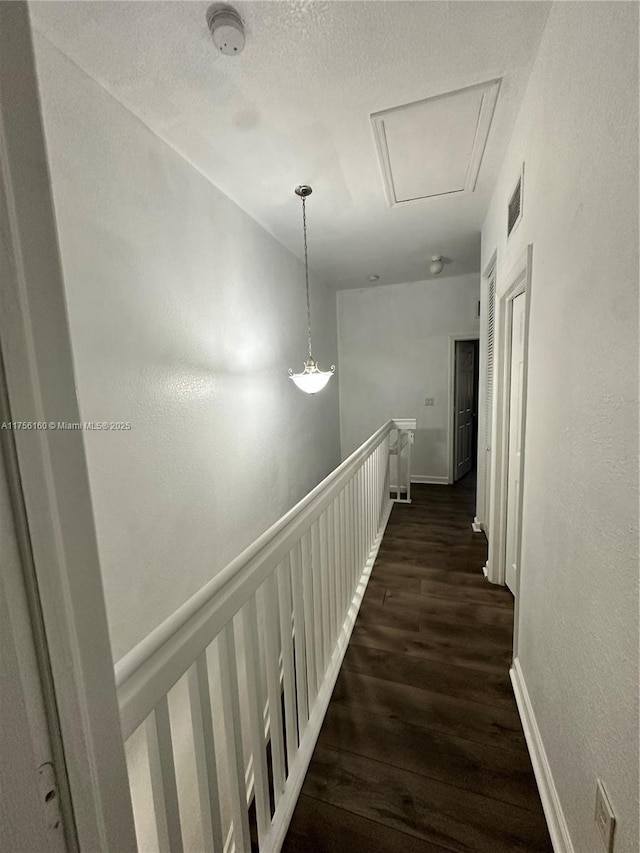 hall with dark wood-style floors, visible vents, a textured wall, a textured ceiling, and an upstairs landing