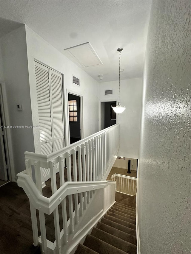 stairs featuring a textured ceiling, a textured wall, and visible vents