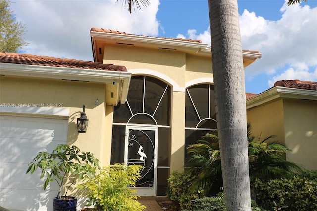 view of exterior entry with a garage, a tiled roof, and stucco siding