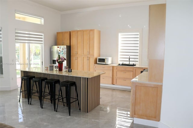 kitchen featuring stainless steel fridge, white microwave, light countertops, crown molding, and light brown cabinetry