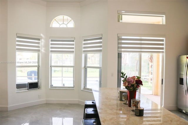 kitchen featuring crown molding, stainless steel refrigerator with ice dispenser, baseboards, and light stone countertops