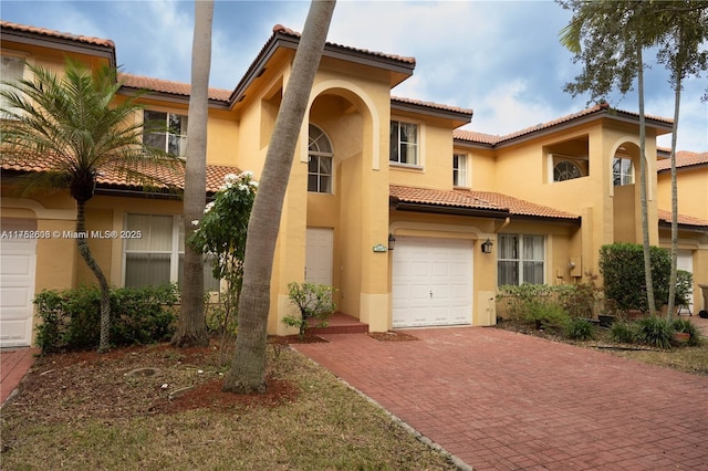 mediterranean / spanish home featuring an attached garage, a tiled roof, decorative driveway, and stucco siding