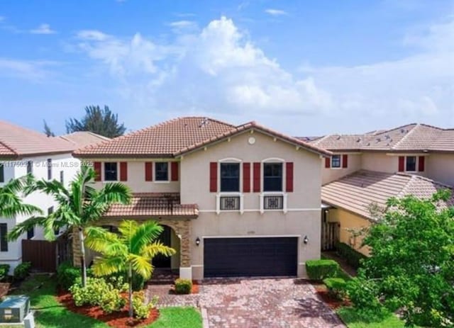 mediterranean / spanish-style house featuring a tiled roof, decorative driveway, an attached garage, and stucco siding