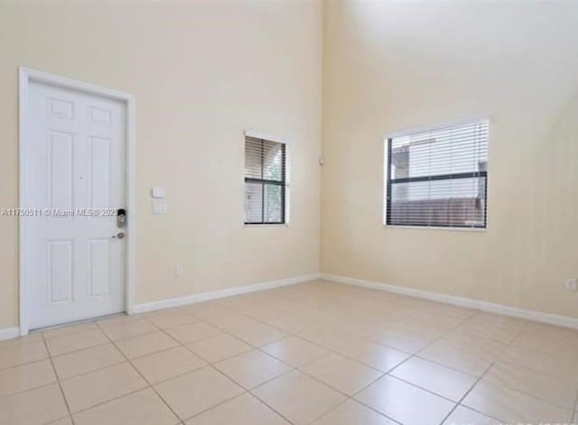 spare room with a high ceiling, light tile patterned flooring, and baseboards