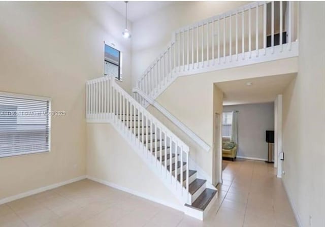 stairway featuring a high ceiling, tile patterned flooring, and baseboards