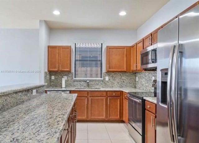 kitchen with a sink, appliances with stainless steel finishes, light stone countertops, tasteful backsplash, and brown cabinetry