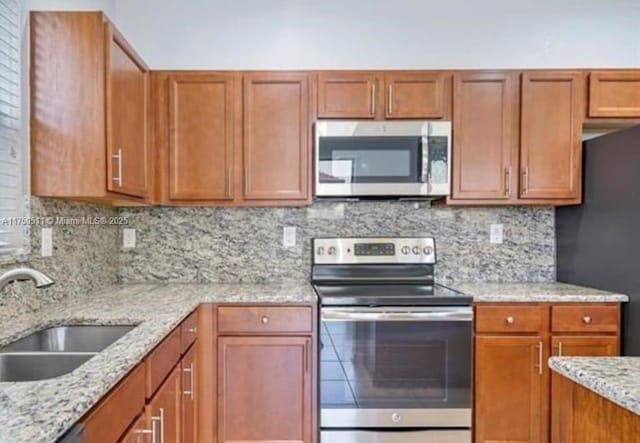 kitchen with decorative backsplash, light stone counters, brown cabinets, appliances with stainless steel finishes, and a sink