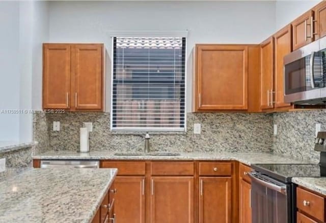 kitchen with stainless steel appliances, a sink, light stone counters, and decorative backsplash