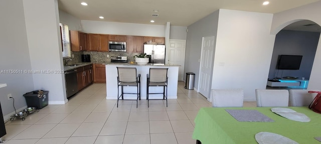 kitchen featuring light tile patterned floors, tasteful backsplash, a kitchen island, stainless steel appliances, and a sink