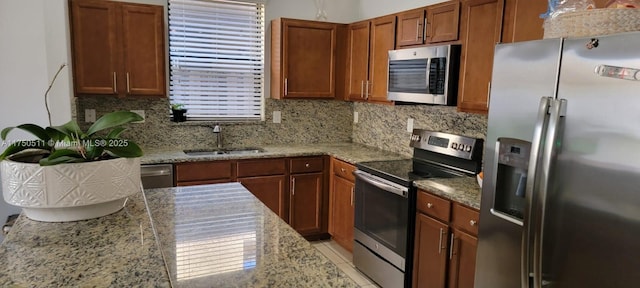 kitchen with appliances with stainless steel finishes, brown cabinets, a sink, and tasteful backsplash