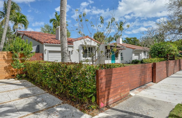 mediterranean / spanish home featuring a garage, a fenced front yard, a tile roof, and stucco siding