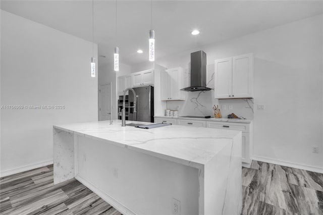 kitchen featuring a kitchen island with sink, white cabinets, freestanding refrigerator, light stone countertops, and wall chimney exhaust hood