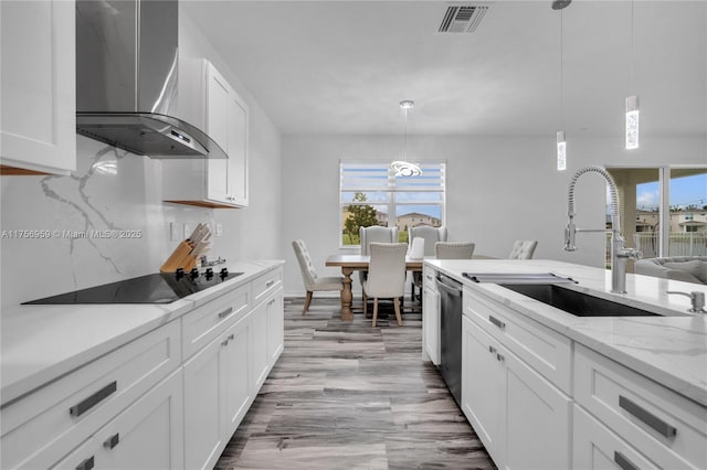 kitchen with black electric stovetop, a sink, white cabinets, stainless steel dishwasher, and wall chimney exhaust hood