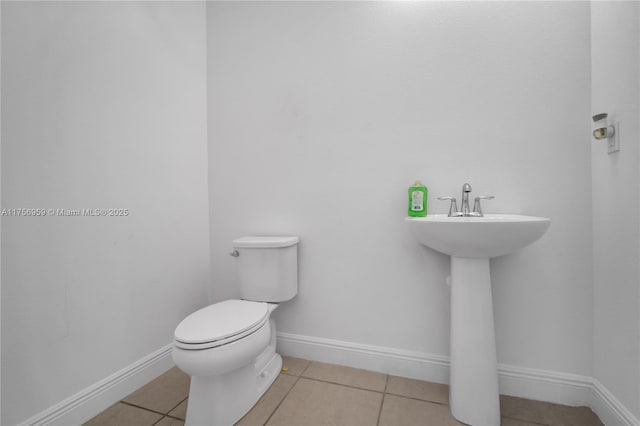 half bathroom with tile patterned flooring, baseboards, a sink, and toilet