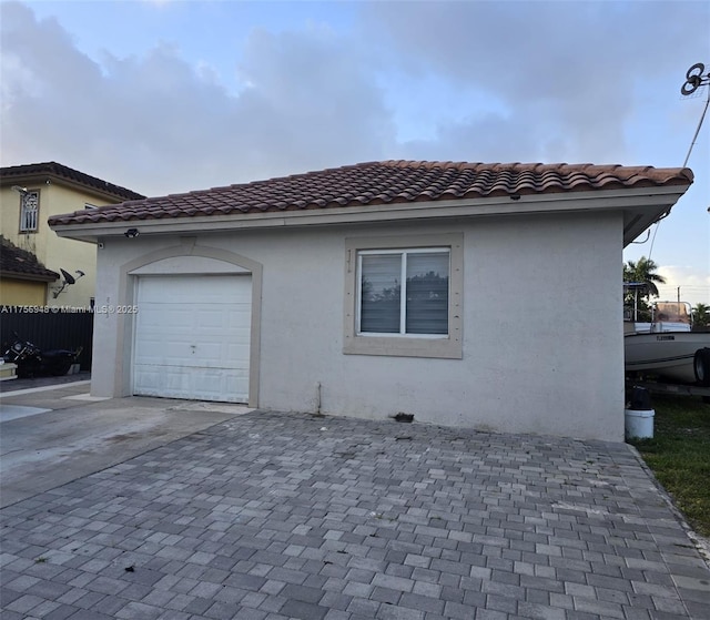 view of side of property with fence, a tiled roof, stucco siding, a garage, and driveway