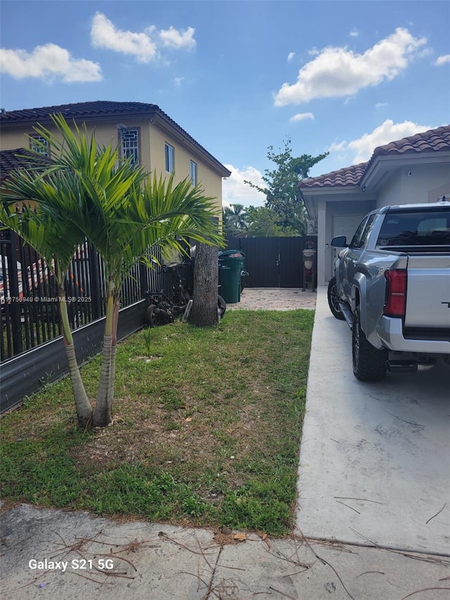 view of side of property featuring a tiled roof, stucco siding, an attached garage, and fence