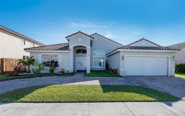 mediterranean / spanish house featuring stucco siding, an attached garage, fence, decorative driveway, and a front yard