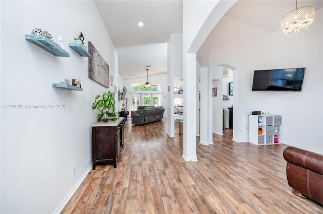 living area featuring arched walkways, baseboards, vaulted ceiling, and light wood finished floors