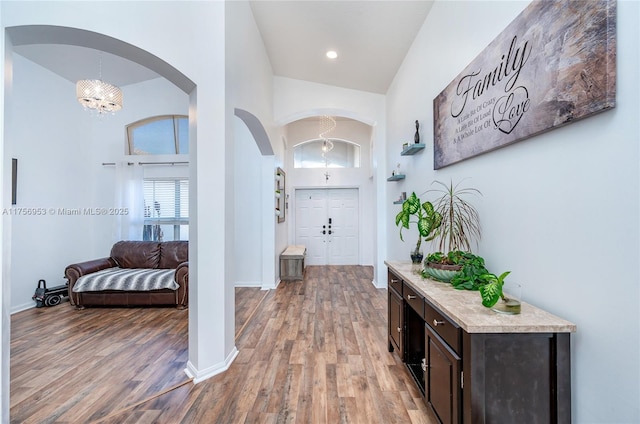 hall with a high ceiling, light wood-style floors, arched walkways, a chandelier, and baseboards