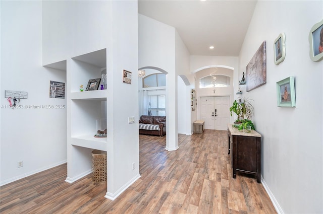 foyer entrance featuring baseboards, arched walkways, a high ceiling, and wood finished floors