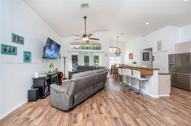 living area featuring a ceiling fan, visible vents, wood finished floors, high vaulted ceiling, and baseboards