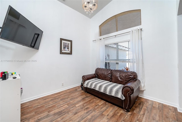 living area with baseboards, an inviting chandelier, wood finished floors, and high vaulted ceiling