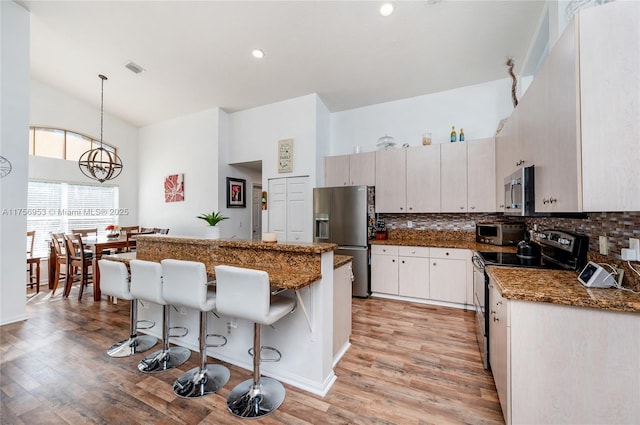 kitchen featuring high vaulted ceiling, a breakfast bar, light wood-style floors, appliances with stainless steel finishes, and decorative backsplash