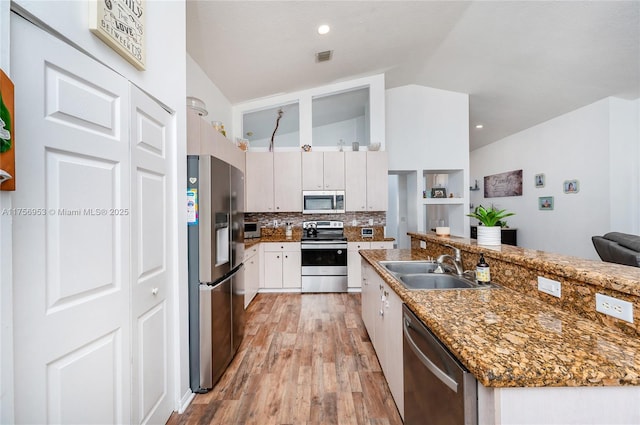 kitchen with appliances with stainless steel finishes, a sink, decorative backsplash, lofted ceiling, and light wood-type flooring