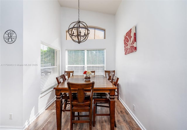 dining area with an inviting chandelier, wood finished floors, a towering ceiling, and baseboards