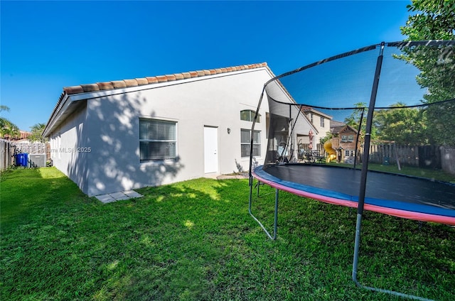 rear view of property featuring a trampoline, fence, a lawn, and stucco siding