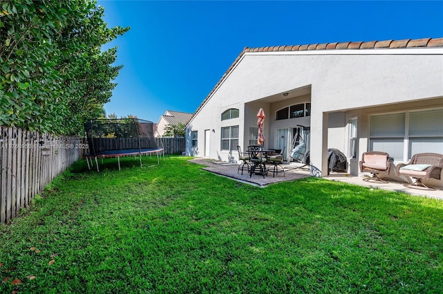 back of house with a fenced backyard, a trampoline, stucco siding, and a yard