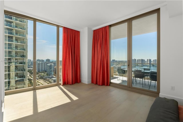 unfurnished room with floor to ceiling windows, a city view, plenty of natural light, and wood finished floors