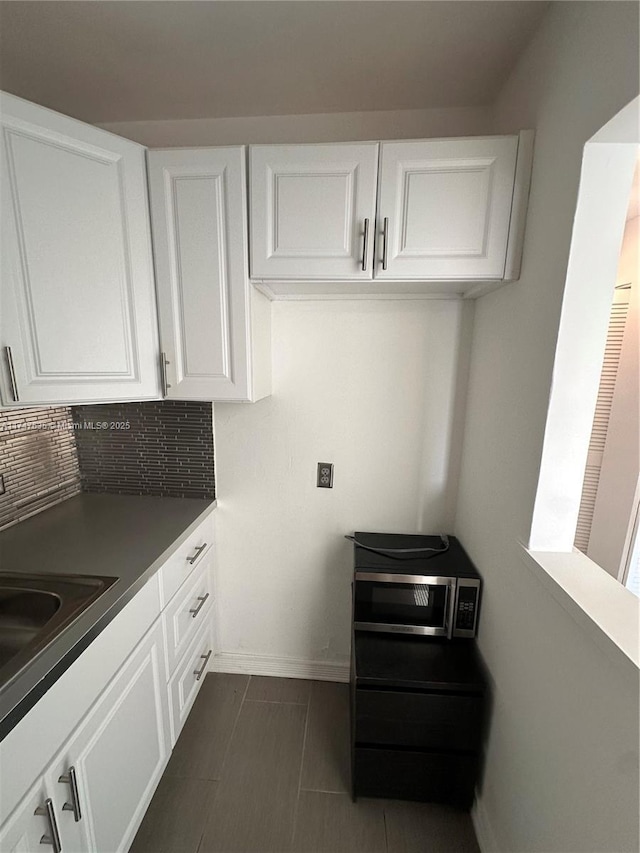 kitchen with tasteful backsplash, white cabinetry, stainless steel microwave, and baseboards