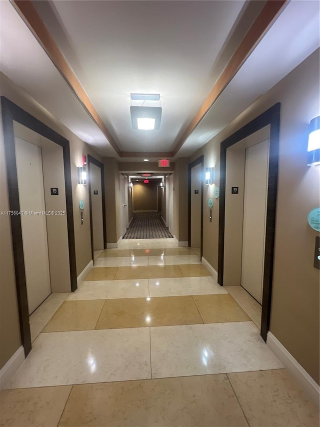corridor with light tile patterned floors, elevator, baseboards, and a raised ceiling