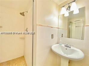 full bath featuring a shower with shower door, a sink, and tile walls