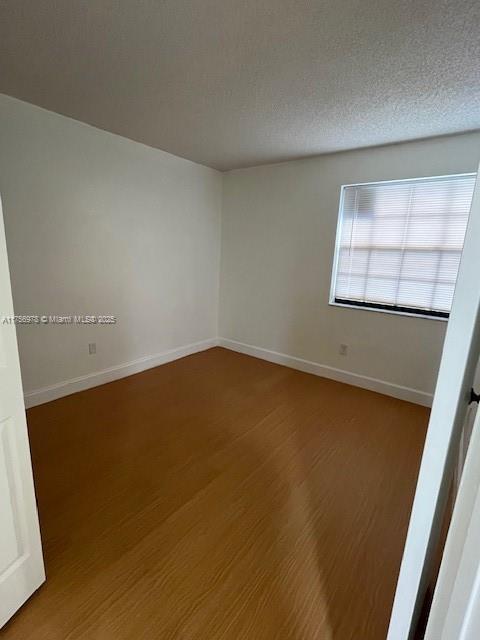 unfurnished room with a textured ceiling, baseboards, and wood finished floors