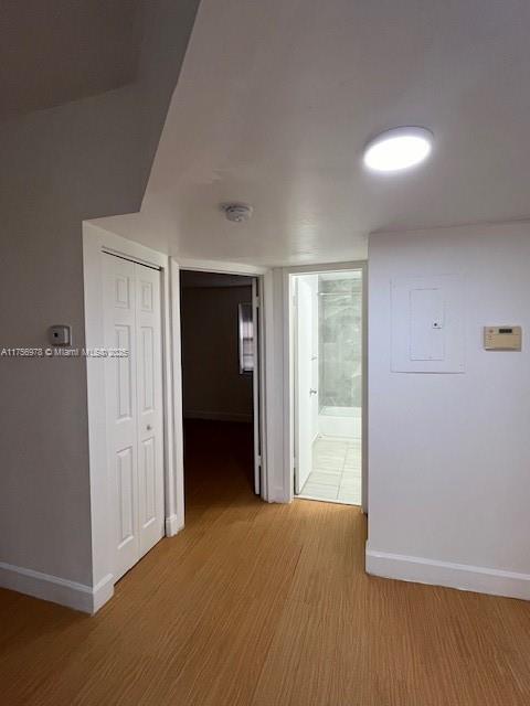 hallway featuring wood finished floors, electric panel, and baseboards