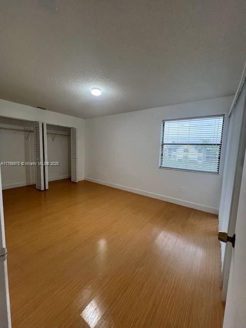 unfurnished bedroom featuring a textured ceiling, multiple closets, light wood-style flooring, and baseboards