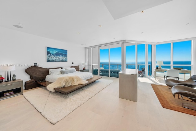 bedroom featuring access to outside, a wall of windows, a water view, and wood finished floors