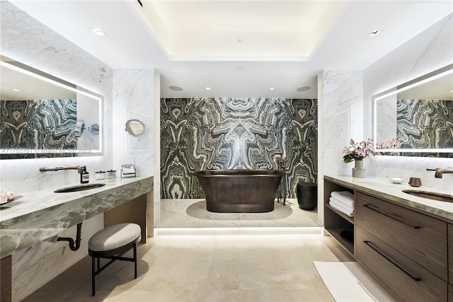 bathroom with a freestanding tub, a raised ceiling, and two sinks