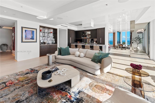 living room featuring a raised ceiling, a bar, and wood finished floors