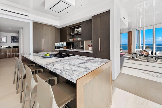 100 S Pointe Dr Unit 2803, Miami Beach, FL 33139 - kitchen with open shelves, a breakfast bar, modern cabinets, dark brown cabinetry, and light stone counters