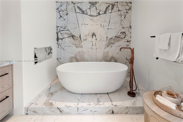 bathroom featuring marble finish floor, stone wall, and a freestanding bath