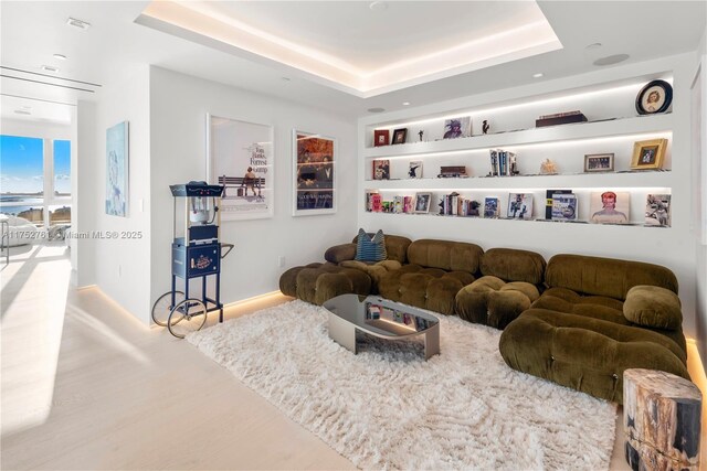 living area with wood finished floors, a raised ceiling, and baseboards