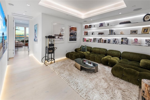 living area with wood finished floors, a raised ceiling, and baseboards