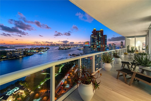 balcony at dusk featuring a city view and a water view