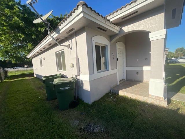 view of property exterior featuring a lawn, a tiled roof, and stucco siding